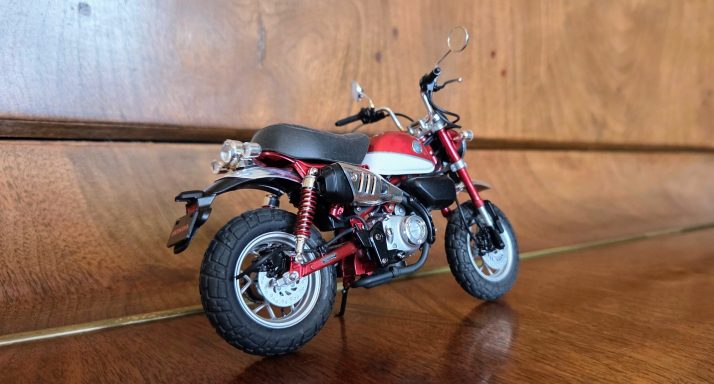 A miniature motorcycle model in red and black, displayed on a wooden surface.