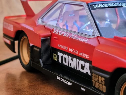 Red Tomica racing car model with detailed features and sponsor logos.