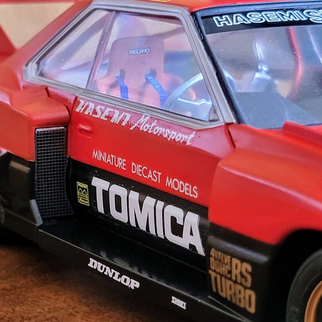 A red model car with "TOMICA" branding and detailed racing features.