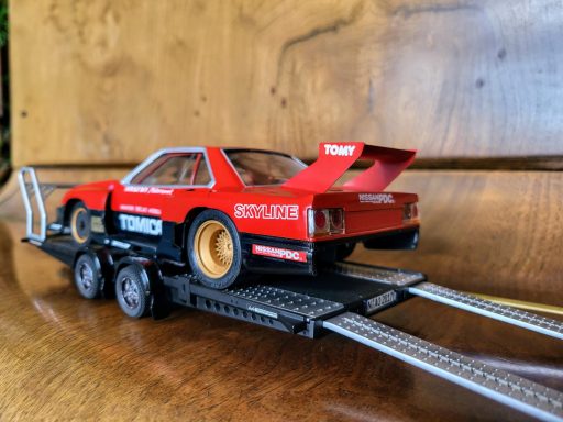 Red classic car model on a black trailer with racing decals.