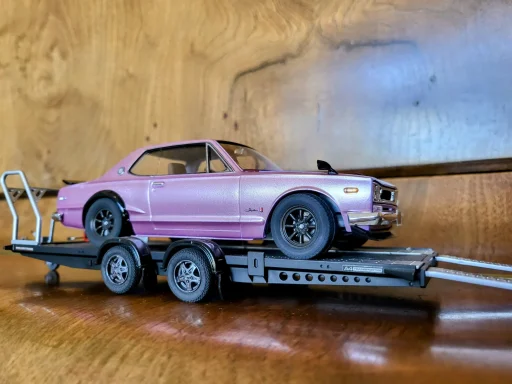 A purple model car on a black trailer against a wooden background.