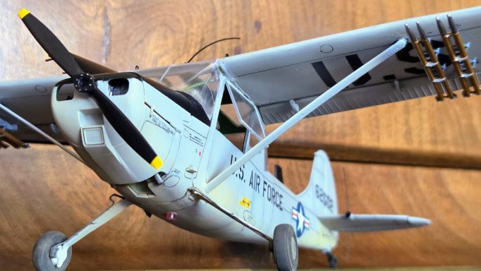 Model of a light aircraft with a grey body and black propeller against a wooden background.